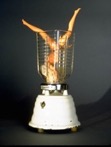 Left, a Barbie doll is positioned upside down inside a metal blender cup, with only her legs and part of her head with messy blonde hair visible. Right, a nude doll is placed upside down in a clear blender jar, with its legs sticking out above the rim.